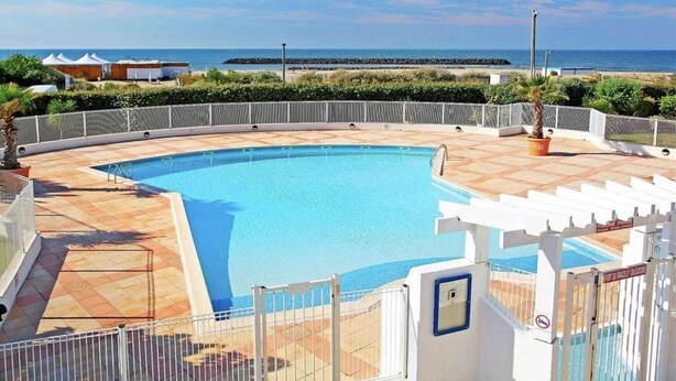 A pool with a view of the sea, a white fence, and a building with a sign. - Studio near the beach - 2 guests (Cap d'Agde)