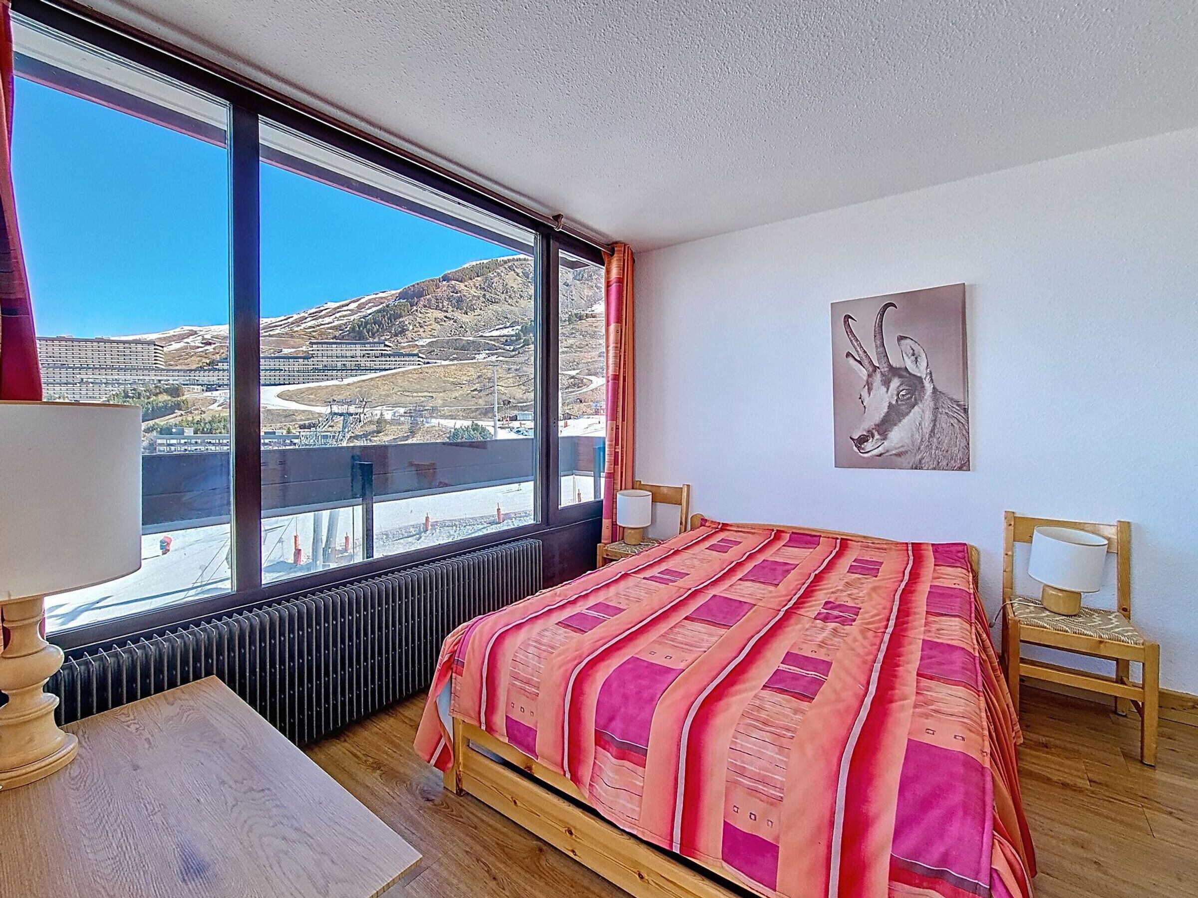 Une chambre avec une grande fenêtre, un lit, une chaise, une table et un radiateur.