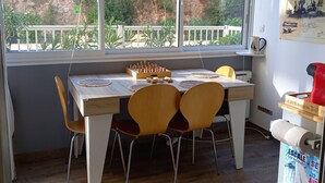 A dining area with a wooden table, four chairs, a chessboard, and a view of a rocky landscape through large windows. - Charming T2 with Terrace and Parking in Sète (Sète)