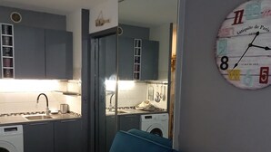 A compact kitchen with a washing machine, a blue sofa, and a wall clock. - Charming T2 with Terrace and Parking in Sète (Sète)