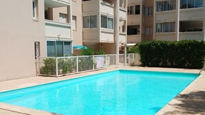 A rectangular swimming pool with a white fence, surrounded by a tiled deck and a building with multiple balconies. - Charming T2 with Terrace and Parking in Sète (Sète)