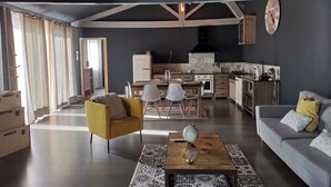 Un vaste espace de vie comprenant une table à manger, des chaises, un canapé et, au fond, une cuisine.