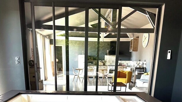 Une salle de bain moderne dotée d’un jacuzzi entouré de parois en verre, d’un espace cuisine ouvert et d’une porte-fenêtre coulissante donnant sur un espace extérieur.