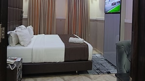 Quarto de hotel moderno com cama, cortinas, televisão e área de estar.