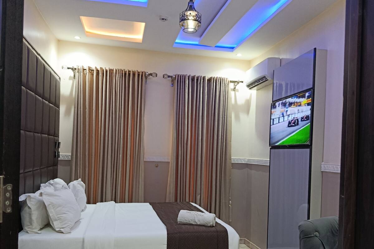 Una habitación de hotel moderna con cama, cortinas, televisión y zona de estar.