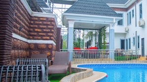 Uma piscina com borda curva, área de estar coberta e um muro de tijolos.