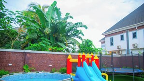 Um quintal com piscina, escorregador inflável e trampolim.