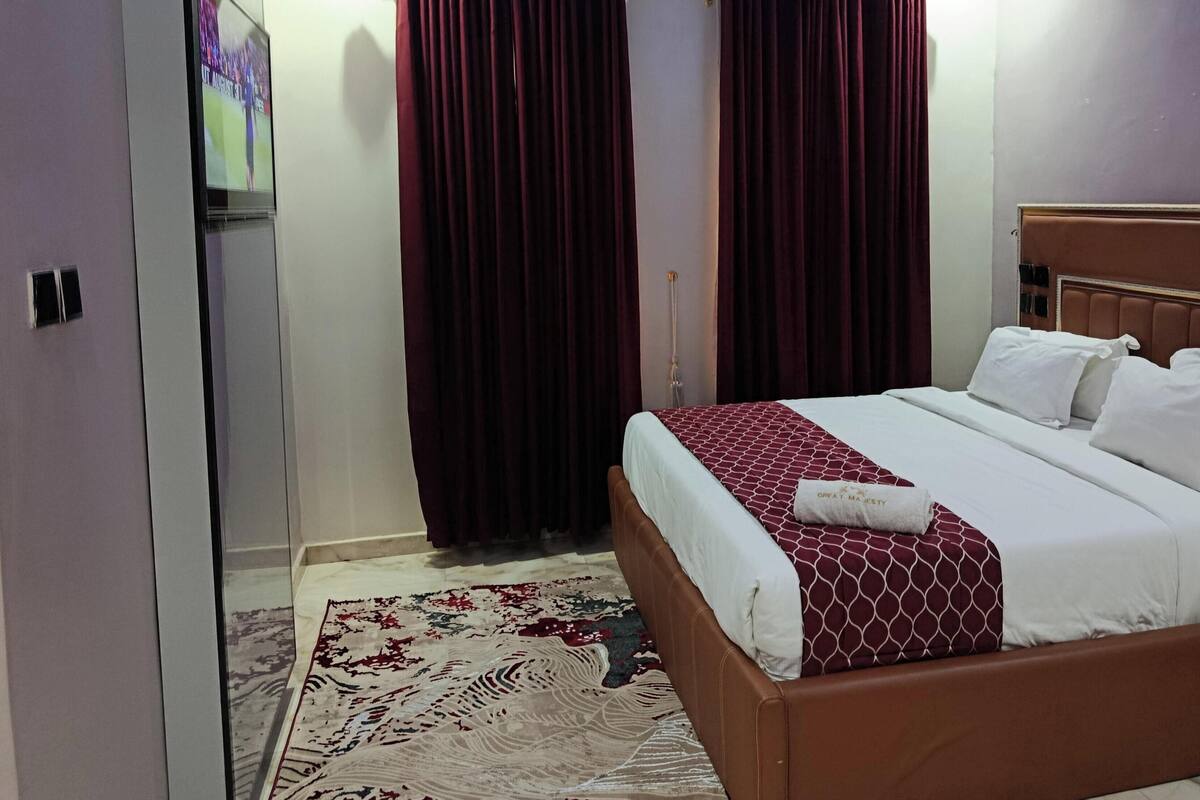 Una habitación de hotel con cama, mesita de noche, lámpara y ventana con cortinas.
