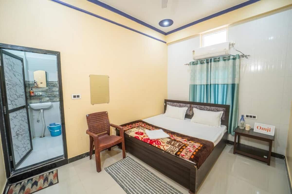 A hotel room with a bed, a chair, a small table, a sink, and a window with curtains.
