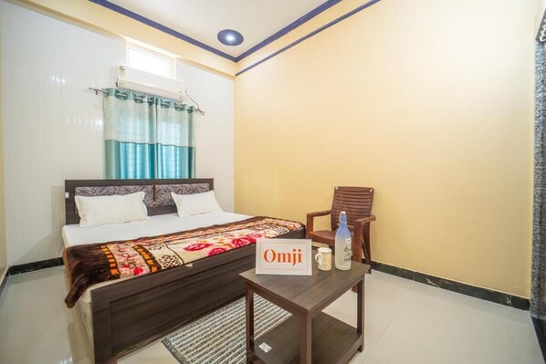 Habitación de hotel con una cama, una silla, una mesita con un cartel y una ventana con cortinas.