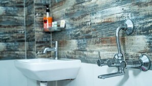 A bathroom with a white sink, a wall-mounted faucet, and a shelf with toiletries. - Omji Ashram - Char Bhuja Dham (Ayodhya)