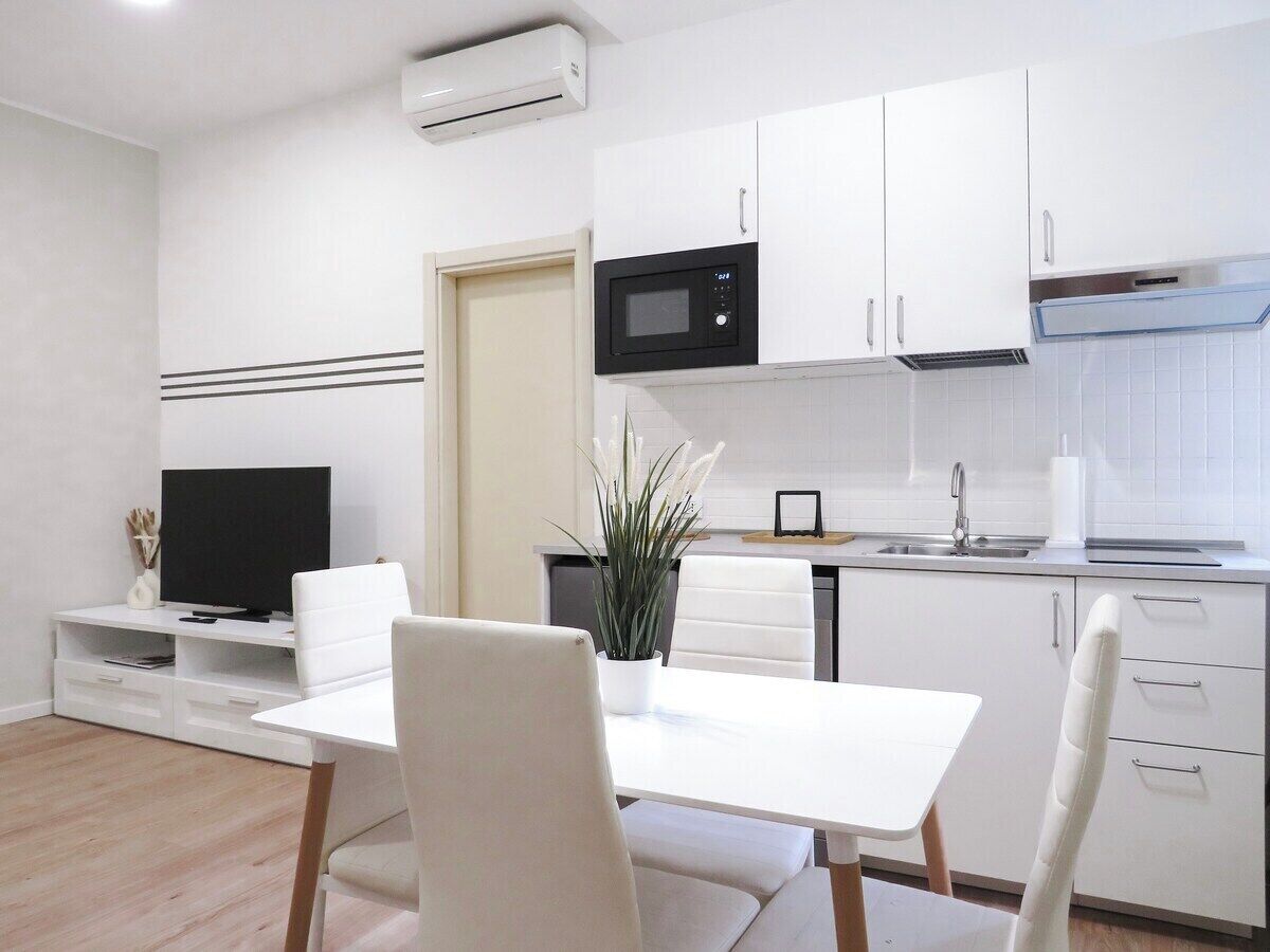 Une cuisine moderne avec des meubles blancs, un four à micro-ondes et un évier. On y trouve également un coin repas avec une table et des chaises blanches.