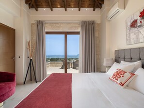 A bedroom with a bed, a red chair, a view of the sea, and a stone wall. - Seaview Luxury Villa In Chania (Kissamos)