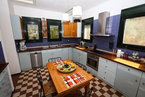 A compact kitchen with a wooden table, a built-in oven, and a window with a view. - Villa Ostria by Rentals Pro Nea Moudania (Nea Moudania)
