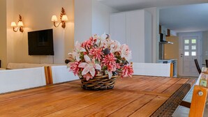 Un comedor con una mesa de madera, un centro decorativo de mimbre y un televisor montado en la pared.
