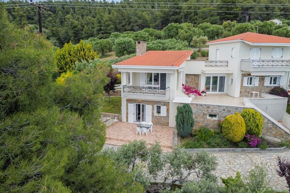 A two-story house with a balcony, a stone pathway, and a garden with various plants.