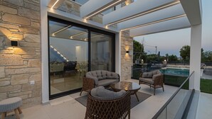 A modern outdoor patio with wicker furniture, a glass table, and a pool. - Villa Amelia by Travel Pro - Mouries Halkidiki (Nea Moudania)