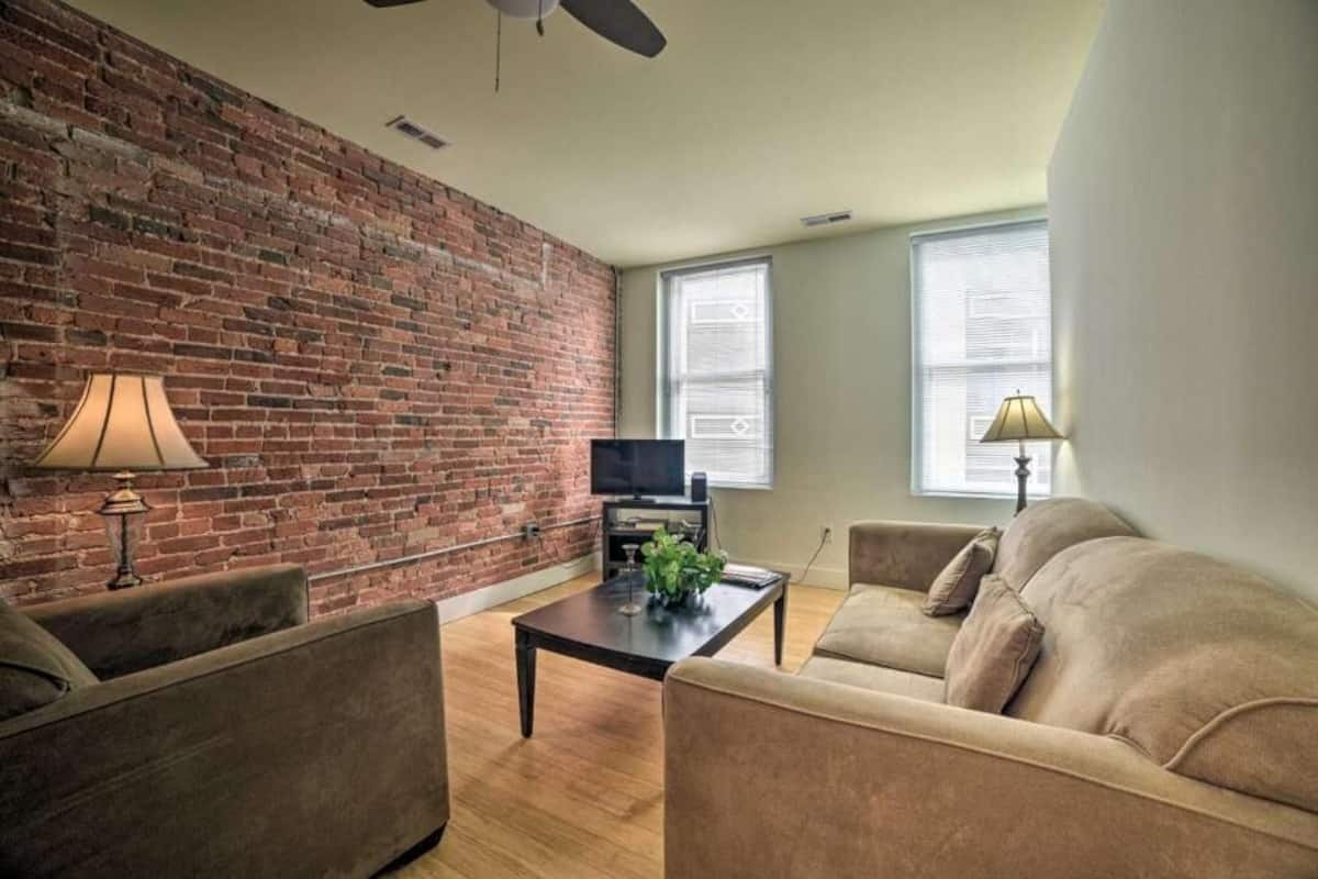 A living room with a brick wall, a television, a coffee table, two sofas, and a ceiling fan.