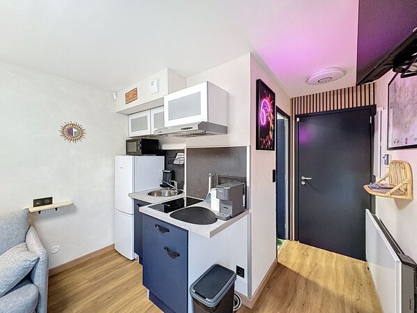 A compact kitchen with white cabinets, a microwave, a sink, and a small trash bin.