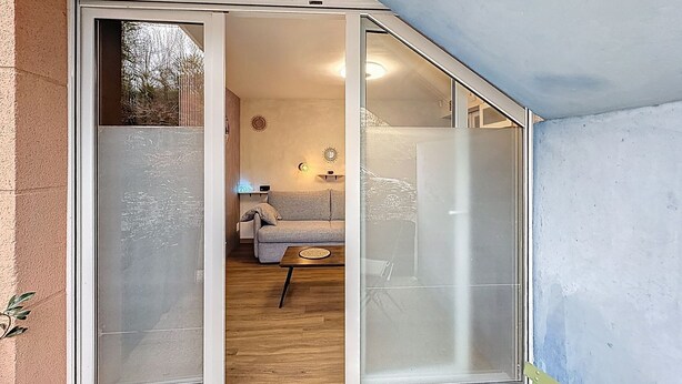 A room with a sliding glass door leading to a living area with a sofa and a small table. - Studio with small terrace on first floor (Amiens)