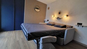 A modern bedroom with a convertible bed, a striped wall panel, and wall-mounted lighting. - Studio with small terrace on first floor (Amiens)