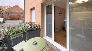 A balcony with a table and bench, a sliding glass door, and a view of a building in the background. - Studio with small terrace on first floor (Amiens)