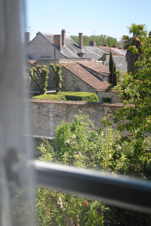 Une vue d’un bâtiment doté d’un mur en pierre et d’un toit recouvert de tuiles, entouré de verdure.