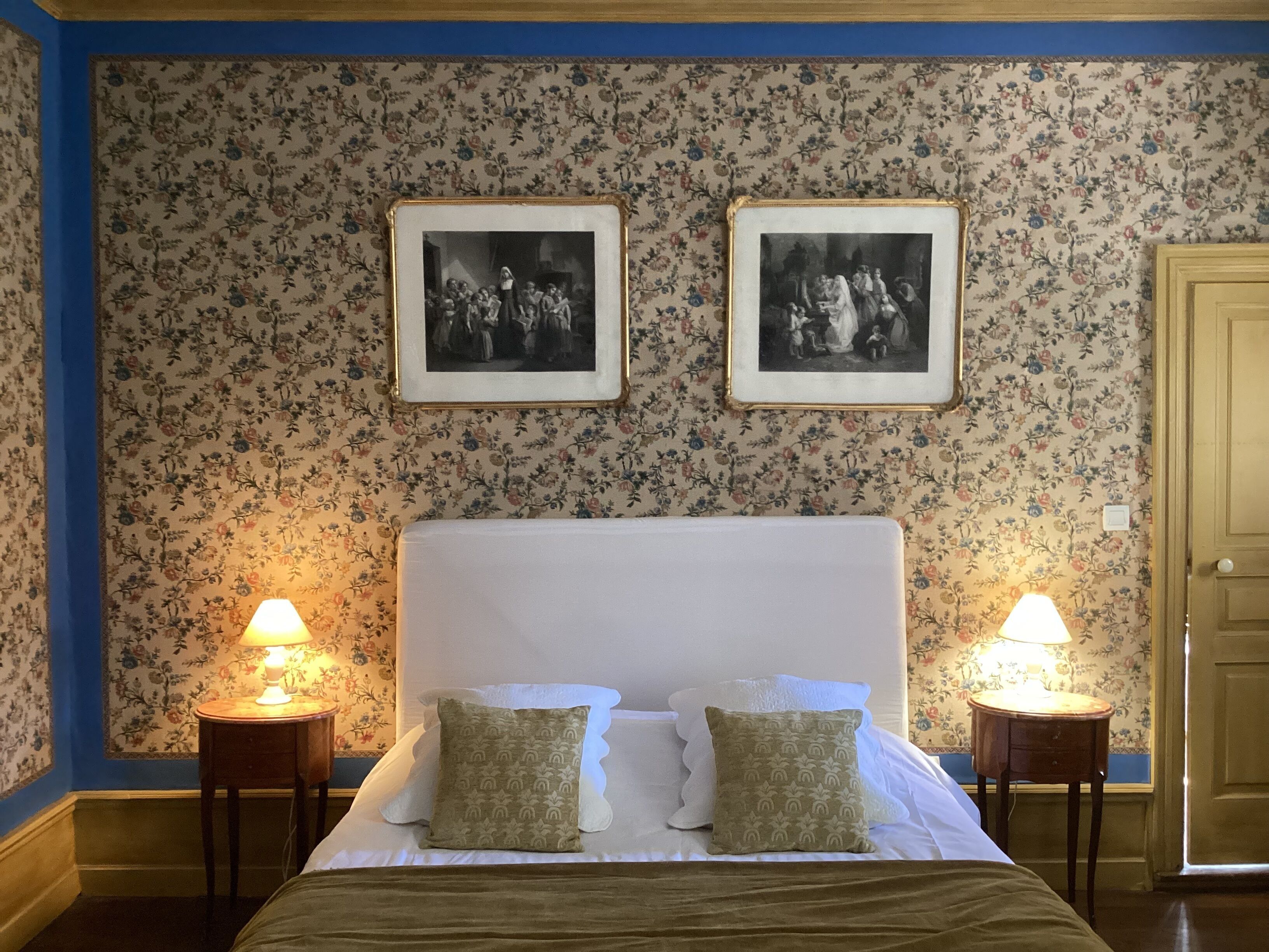 A bedroom with a large bed, two bedside tables, and floral wallpaper.
