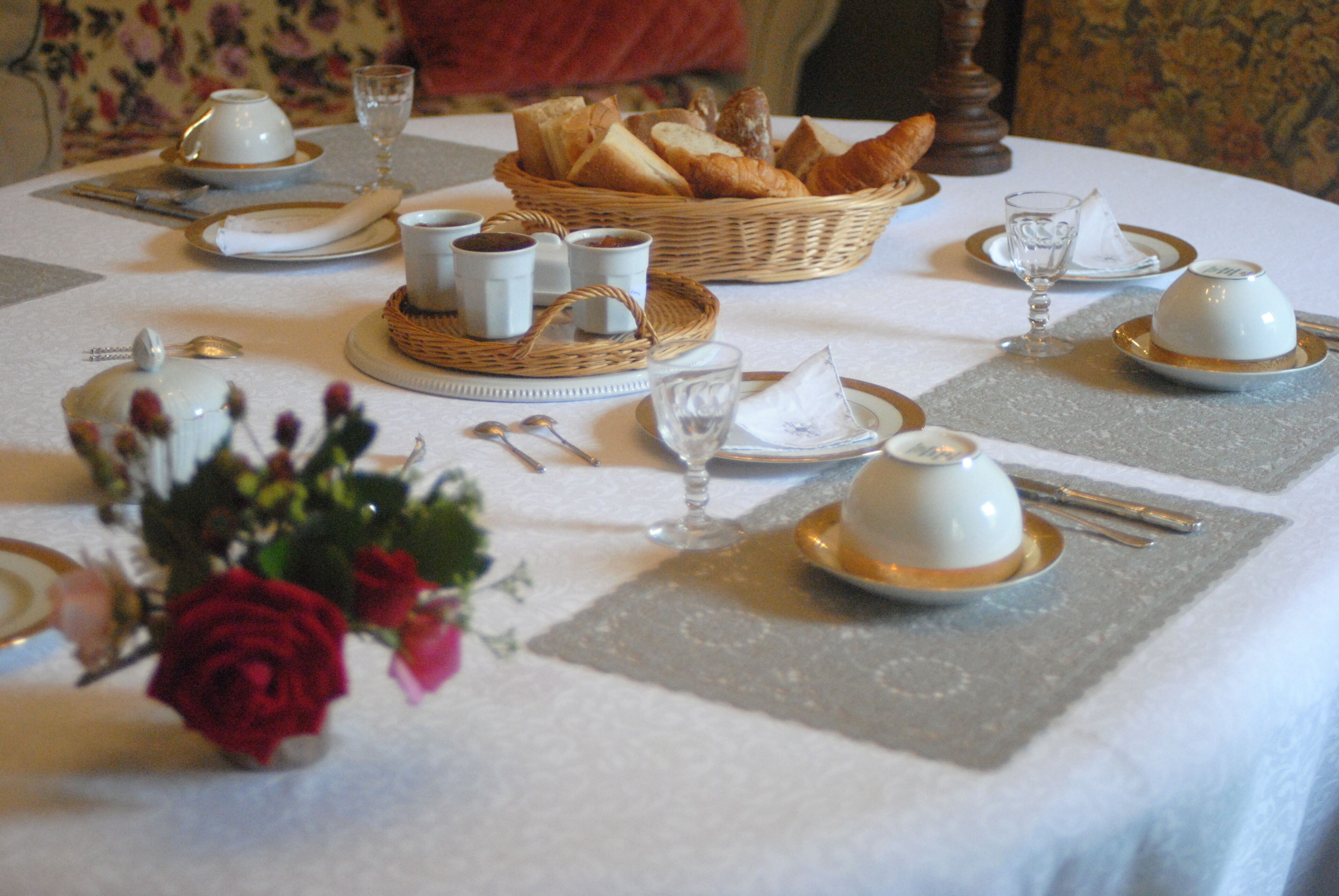 A table set for a meal with bread, cups, and a vase of flowers.