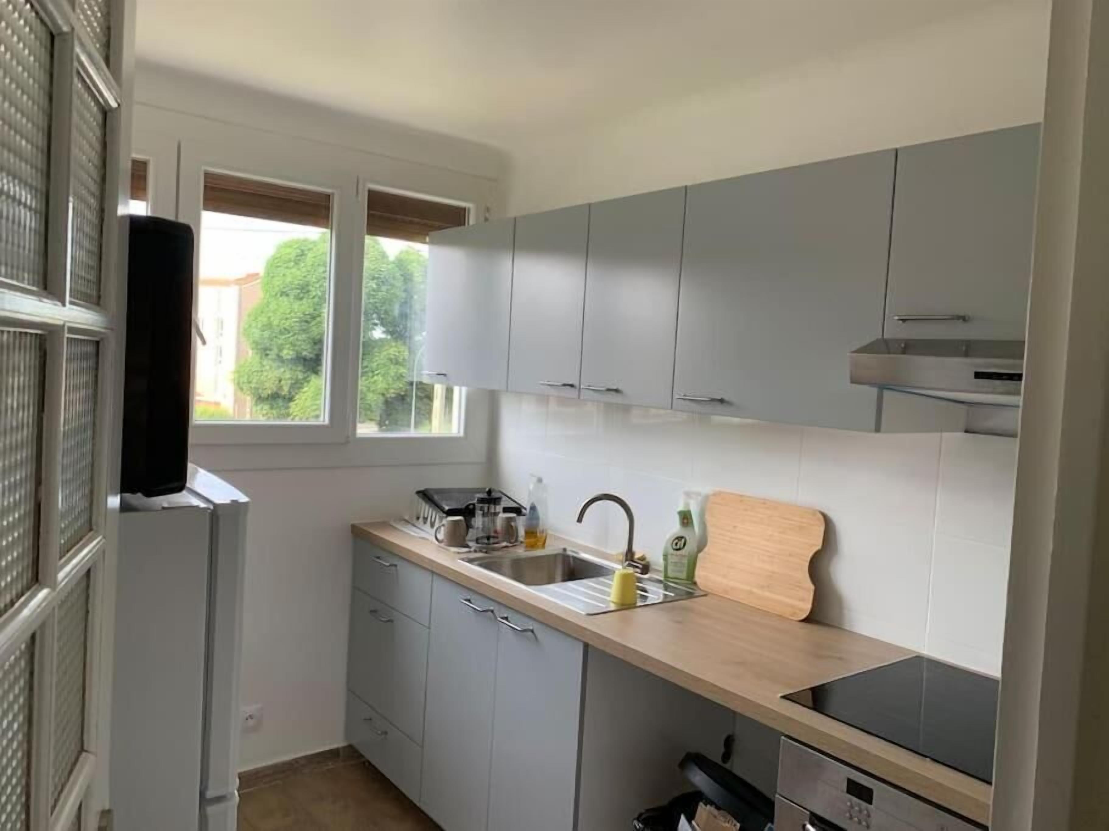 Cocina compacta con armarios grises, encimera de madera, pileta y ventana con vista a follaje.