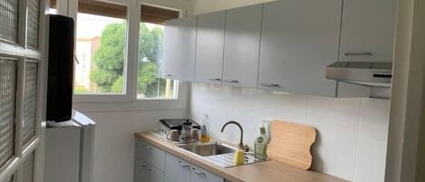 Cocina compacta con armarios grises, encimera de madera, pileta y ventana con vista a follaje.