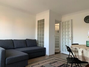 A living room with a grey sofa, a dining table with chairs, and a clock on the wall. - Superbe T3 spacieux (Vigneux-sur-Seine)