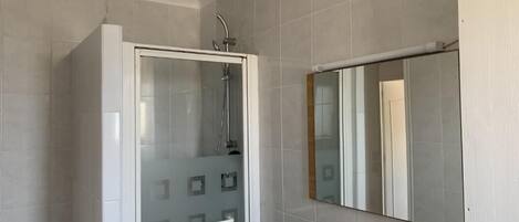 A bathroom with a glass-enclosed shower, a white sink, a mirror, and a towel rack.