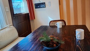 A wooden dining table with a white mug, a bowl of pinecones and greenery, a television mounted on the wall, and a window with curtains. - Casa 2 en Bariloche en un Barrio residencial muy tranquilo cerca de todo (San Carlos de Bariloche)