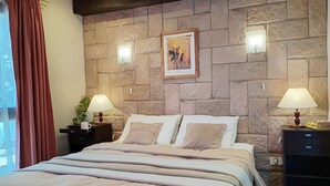 A bedroom with a stone wall, a bed with multiple pillows, bedside lamps, and a nightstand with a plant. - Casa 2 en Bariloche en un Barrio residencial muy tranquilo cerca de todo (San Carlos de Bariloche)