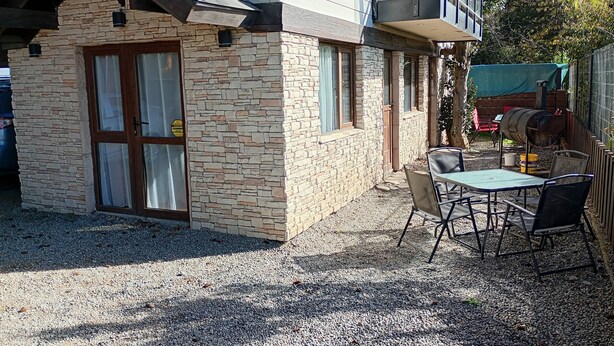 A stone building with a wooden door, a balcony, and a gravel patio with a table and chairs. - Casa 2 en Bariloche en un Barrio residencial muy tranquilo cerca de todo (San Carlos de Bariloche)
