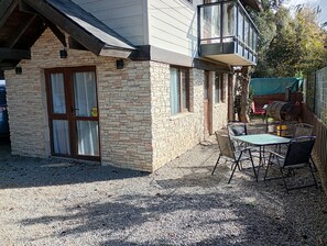 Un edificio de piedra con puerta de madera, balcón y patio de grava con mesa y sillas.