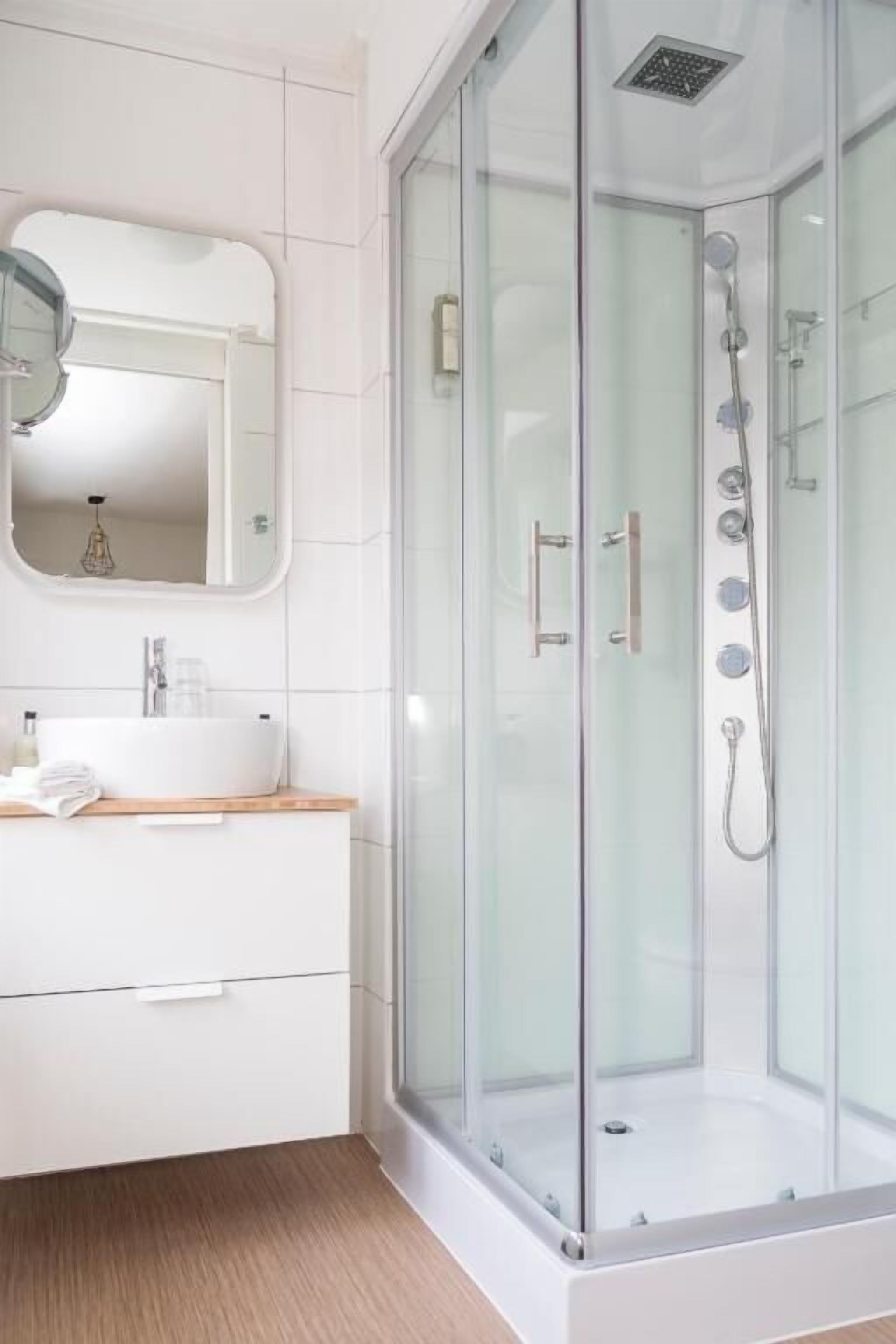 Un bagno moderno con cabina doccia in vetro, un mobile lavabo bianco con specchio e un piano d'appoggio in legno.