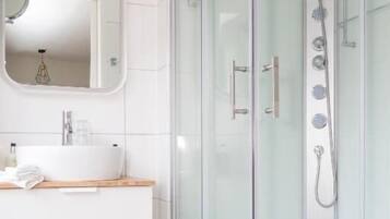Un bagno moderno con cabina doccia in vetro, un mobile lavabo bianco con specchio e un piano d'appoggio in legno.