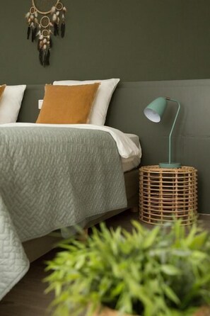 A bed with a textured blanket, a bedside lamp on a woven side table, and a wall-mounted dreamcatcher. - Hotel Vier Jaargetijden (Epen)