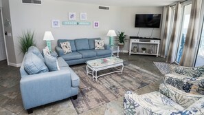 A living room with a sofa, a coffee table, a TV, and a sign that says 'BEACH HOUSE'. - E1401 Stunning Pool/Gulf View, 3 Pools, Tennis, Gym (Panama City Beach)