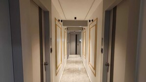 A hotel hallway with doors on both sides, a tiled floor, and a light-colored ceiling.