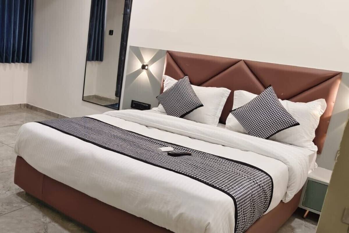 Un dormitorio ordenado con cama, mesita de noche, espejo y ventana con cortinas.