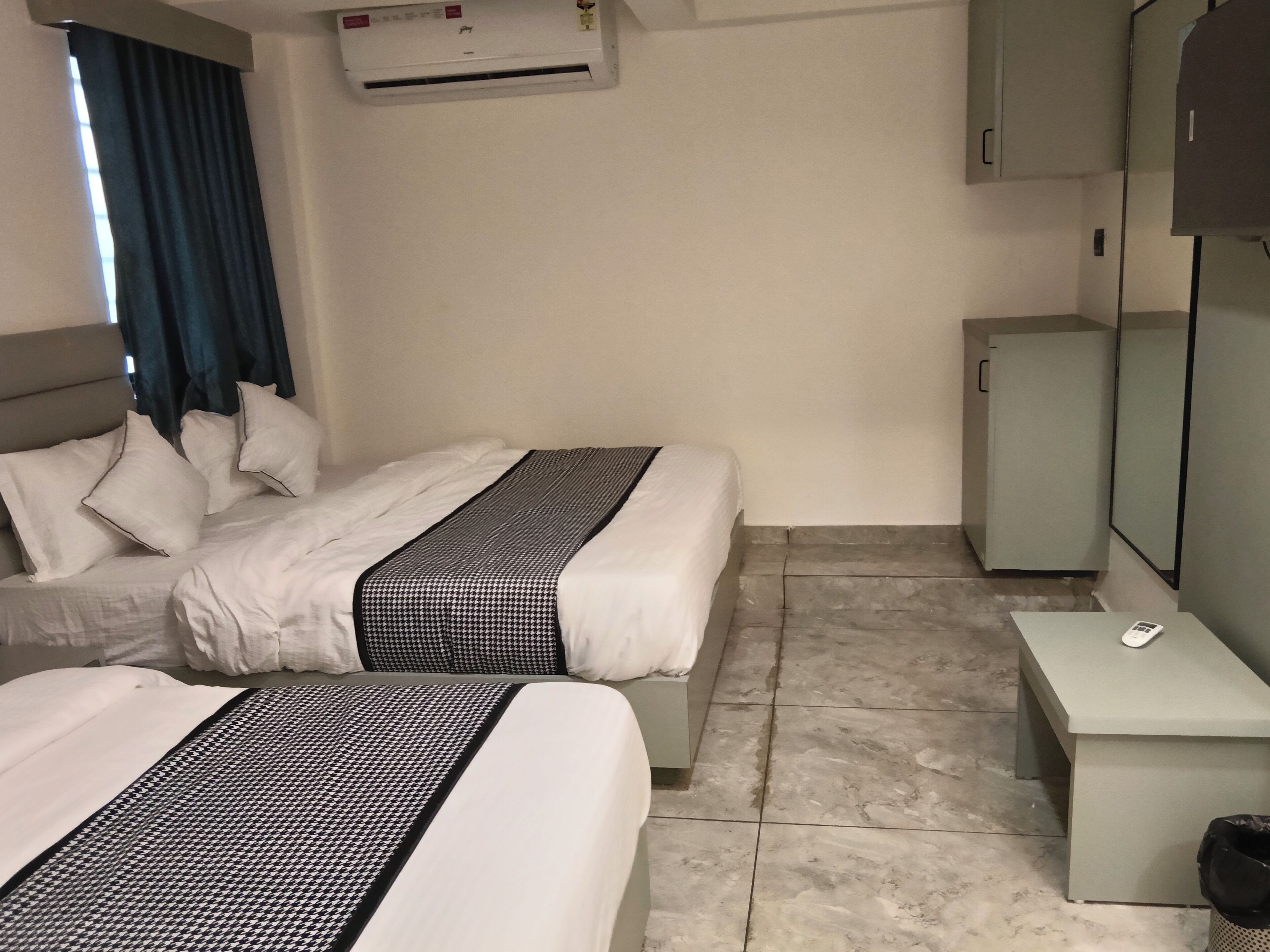 Habitación de hotel con dos camas, una mesita, un espejo, un armario y un equipo de aire acondicionado.