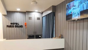 A hotel reception area with a modern design, a reception desk, a flat-screen TV, and a sign that reads 'HOTEL PARIS GRAND'.