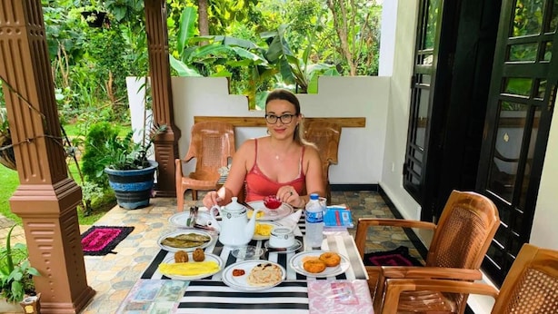 A person seated at a table with a variety of dishes, a teapot, and a water bottle. - Aloe Home Stay (Sigiriya)