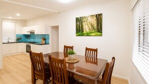 Een eethoek met een houten tafel en stoelen, een keuken op de achtergrond en wanddecoratie met een bosmotief.
