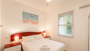 Een net opgemaakt bed met witte lakens, een rood hoofdeinde en een nachtkastje met een lamp.