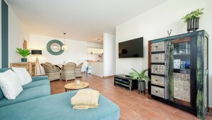 Ein Wohnzimmer mit einem türkisblauen Sofa, Korbstühlen, einem Couchtisch und einem an der Wand befestigten Fernseher.