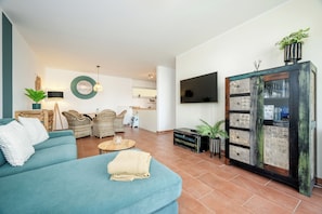 A living room with a teal sofa, wicker chairs, a coffee table, and a TV mounted on the wall. - Wellness apartment in TOP location, close to the beach with sauna and whirlpool. (Nordseeheilbad Schillig)